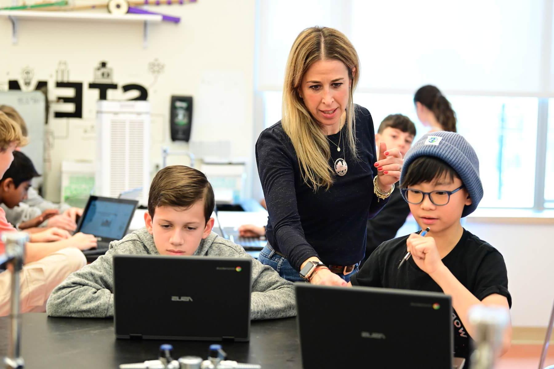 Ethical Culture Fieldston School Middle School students looking at computer with Teacher looking over shoulder to help