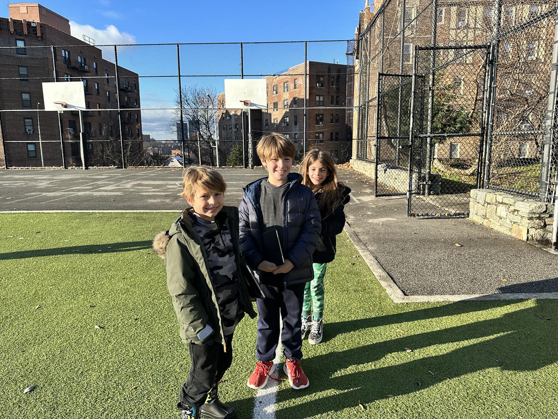 Three Fieldston Lower students pose and smile outdoors on the lower field.