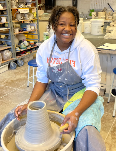 Fieldston Upper student poses and smiles while working on ceramics project in art studio.